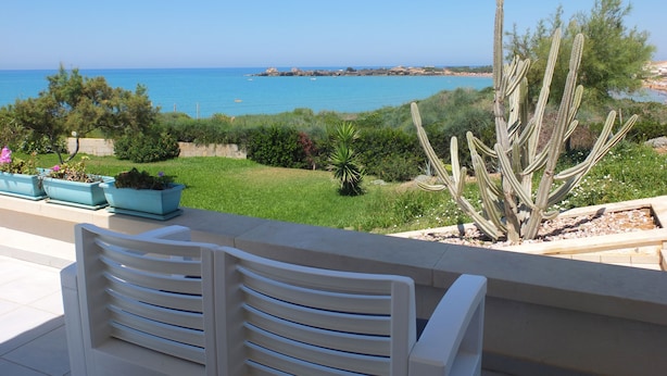 Pátio com cadeiras brancas com vista para um jardim e para o litoral.