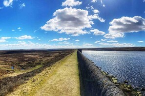 Un paysage côtier avec un mur de pierre menant à une étendue d’eau, sous un ciel dégagé.