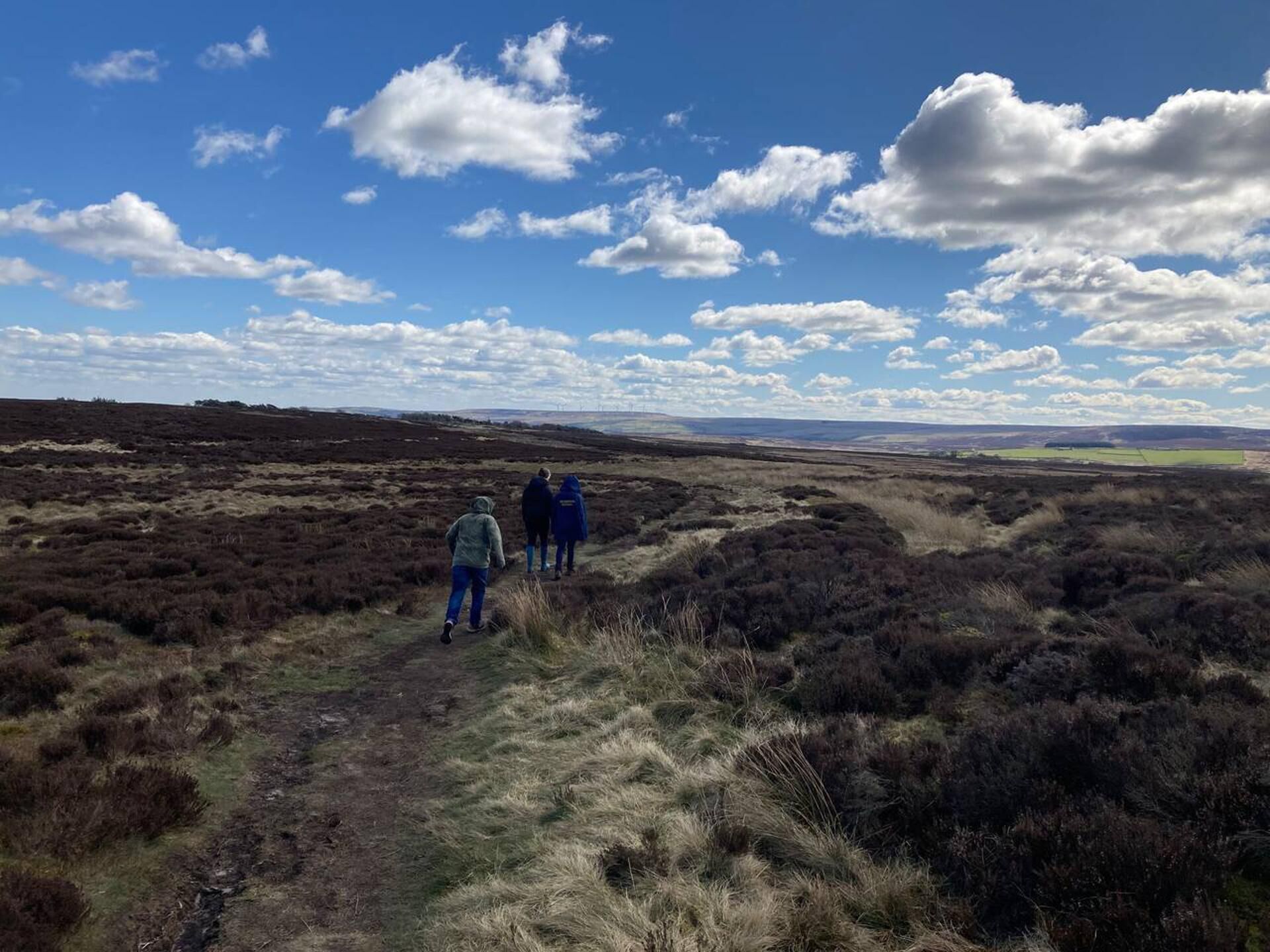 A group of people walking on a path through a natural landscape with a clear sky and distant fields.