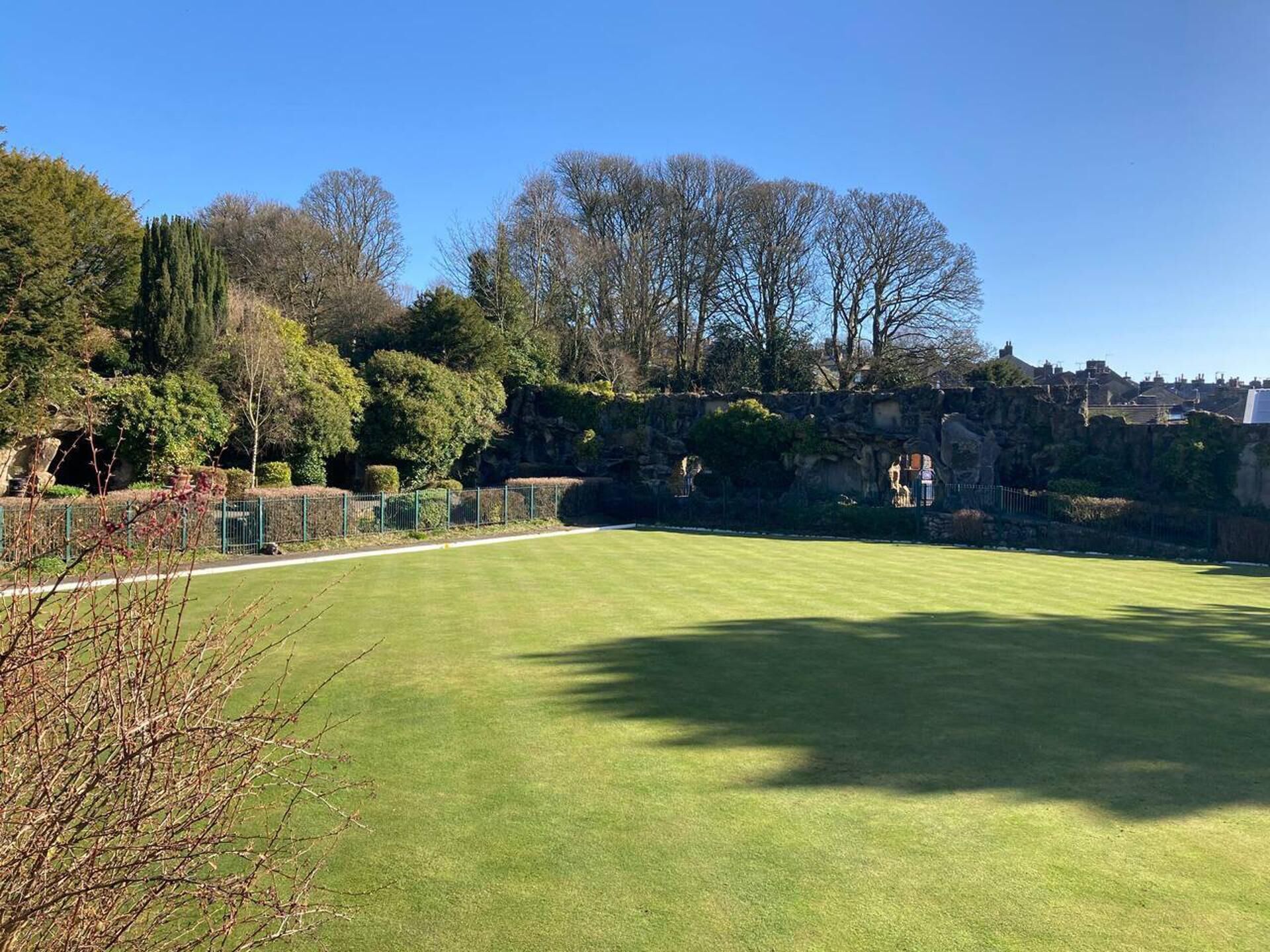 A well-maintained lawn with a stone wall and trees in the background.