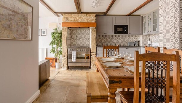 Une cuisine avec une cheminée en pierre, un dosseret carrelé et une table à manger en bois.
