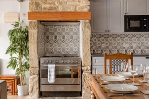 Una cocina con pared de piedra, azulejos estampados, estufa de acero inoxidable y una mesa de comedor preparada para dos.