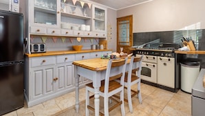 A kitchen with white cabinetry, a wooden table, and a stove. - Cartref - Beautiful Cottage Hot Tub Countryside Views (Saundersfoot)