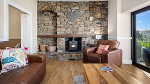 A cozy living room with a stone fireplace, leather sofa, and a wooden coffee table. - Cartref - Beautiful Cottage Hot Tub Countryside Views (Saundersfoot)