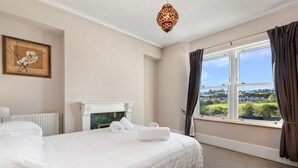 A hotel room with a large bed, a fireplace, a view of the countryside, and a chandelier. - Cartref - Beautiful Cottage Hot Tub Countryside Views (Saundersfoot)