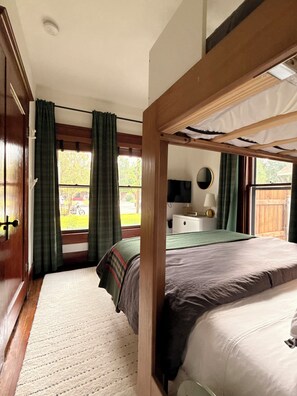 A room with a bunk bed, a desk, a chair, a television, and a window with curtains.