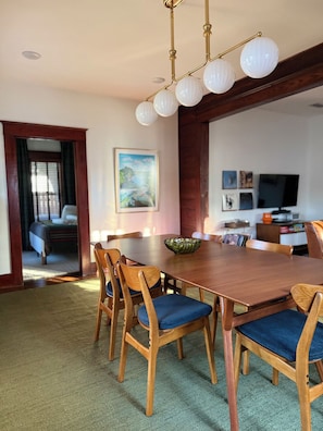 A dining area with a wooden table and chairs, a chandelier, and a painting on the wall. - Boutique Historic Home • Walk Downtown • Sleeps 6 (New Braunfels)