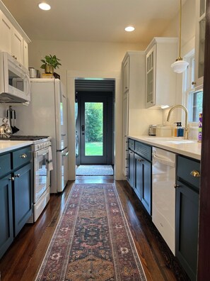 A kitchen with a central island, a view through the door, and a patterned rug. - Boutique Historic Home • Walk Downtown • Sleeps 6 (New Braunfels)