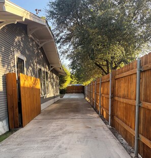 A covered concrete driveway leading to a building with a wooden fence on one side. - Boutique Historic Home • Walk Downtown • Sleeps 6 (New Braunfels)