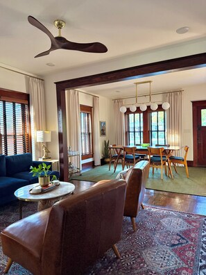 A spacious living area with a ceiling fan, a dining table with chairs, a sofa, and a coffee table with a plant. - Boutique Historic Home • Walk Downtown • Sleeps 6 (New Braunfels)