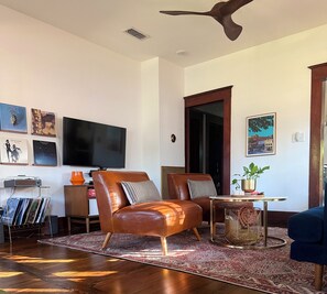 A living room with a brown leather sofa, a television, and a ceiling fan.