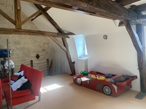 A room with exposed wooden beams, a red chair, a toy car bed, and a stone wall. - La Douce France-Trianon : Chic et élégance (Chinon)