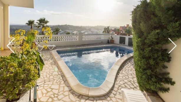 Une piscine dotée d’une terrasse carrelée, entourée de plantes en pot et d’une clôture blanche.