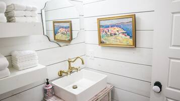 Une salle de bain avec un lavabo blanc, un robinet doré, un miroir et deux tableaux encadrés accrochés au mur.