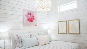 A bedroom with a white wooden wall, a bed with striped bedding, a pink abstract painting, and two framed botanical prints. - "Pigs Fly" an Adorable Guest Suite in the Round Top Area  (Burton)