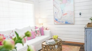 A white wooden room with a white sofa, a glass coffee table, and a painting on the wall. - "Pigs Fly" an Adorable Guest Suite in the Round Top Area  (Burton)