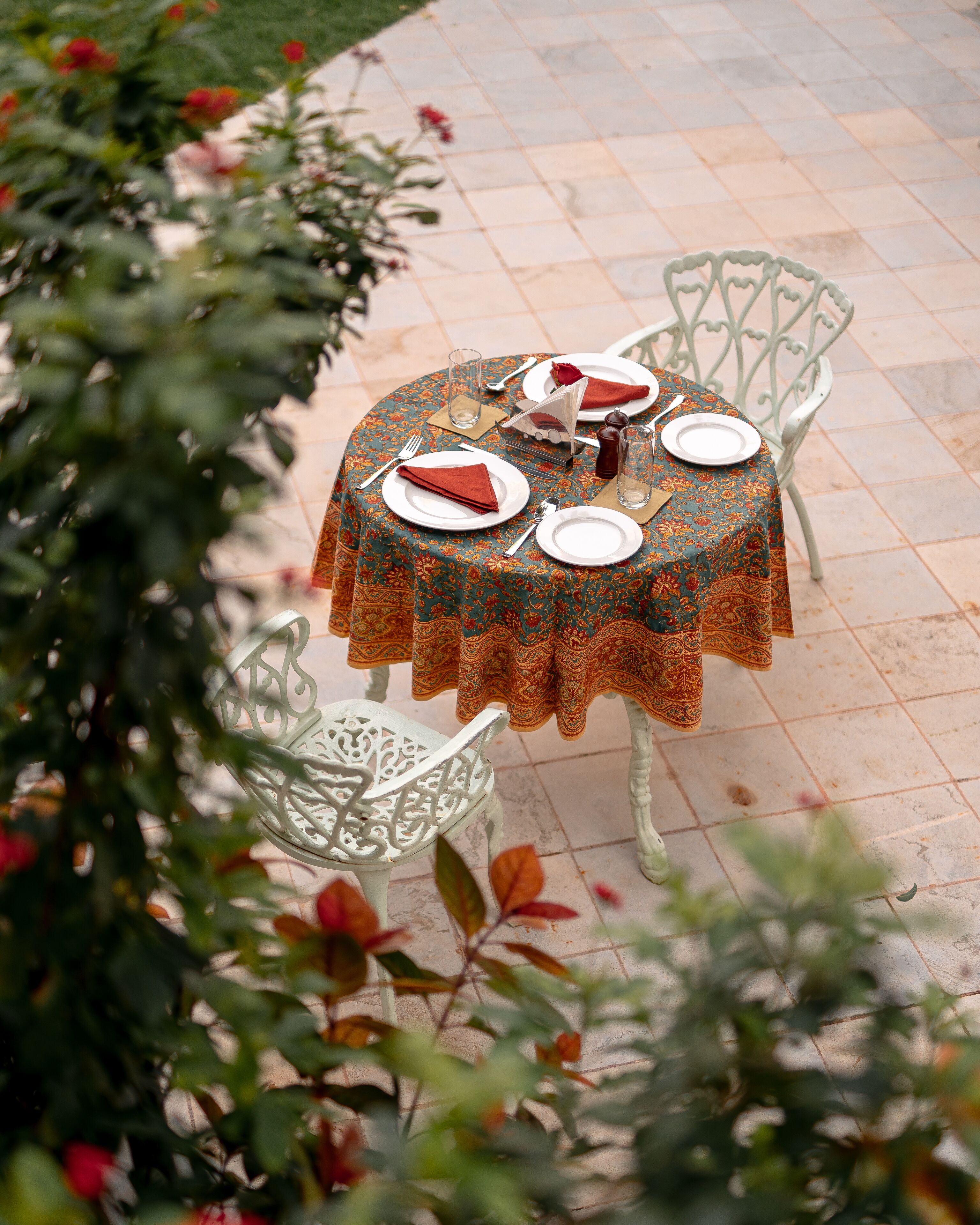 An outdoor dining area with a round table set for two, surrounded by white chairs.