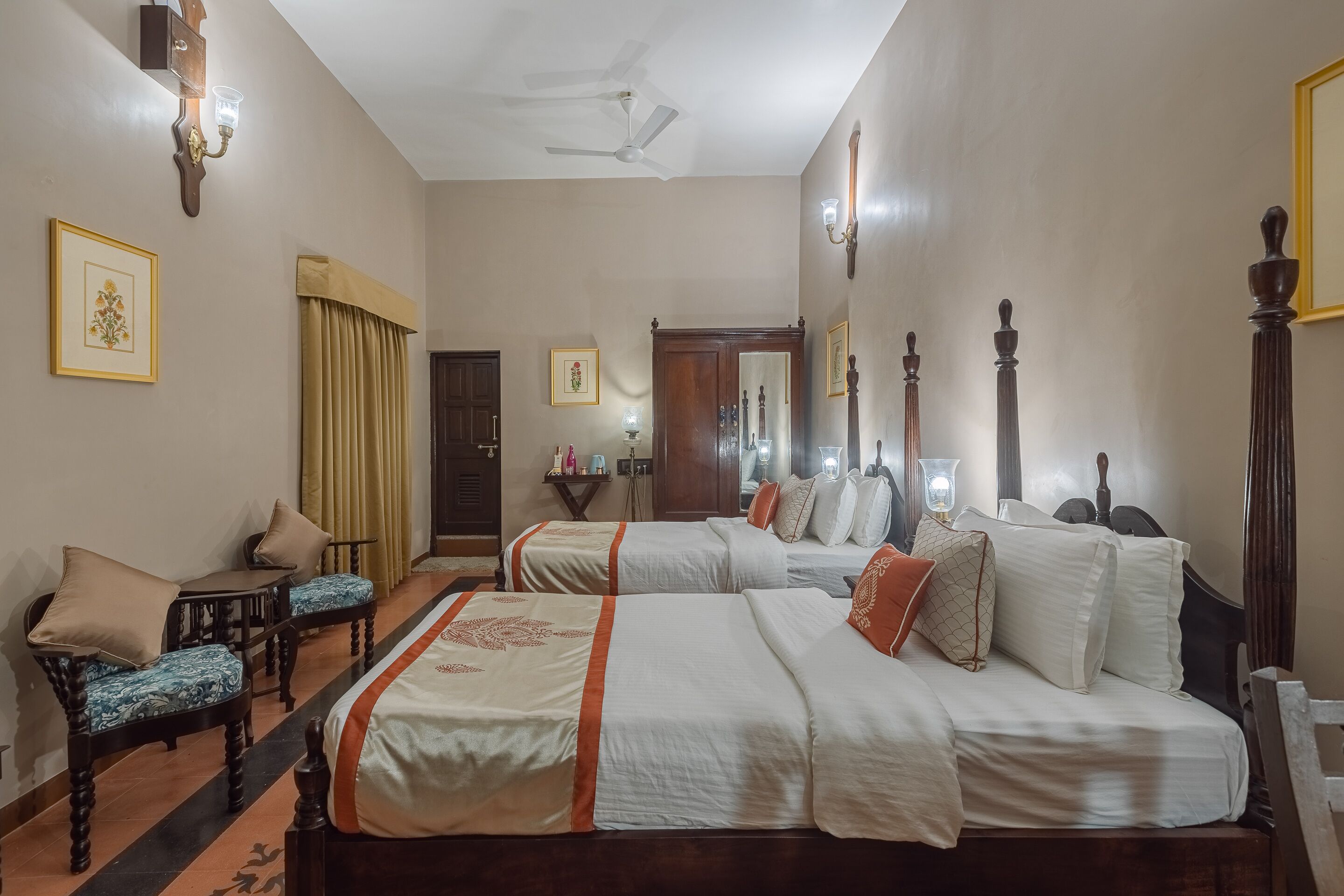 A hotel room with two beds, a sitting area with a chair and table, a ceiling fan, and a mirror.