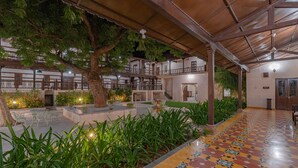A covered courtyard with a tiled floor, outdoor seating, and a tree providing shade. - Tree of Life Darbargadh, Dared (Vav)