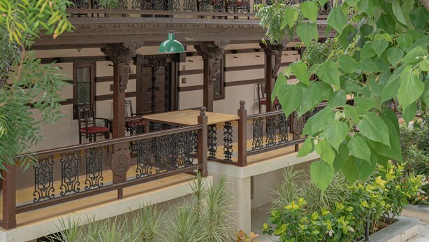 A multi-story building with balconies, wooden railings, and a garden area with various plants. - Tree of Life Darbargadh, Dared (Vav)