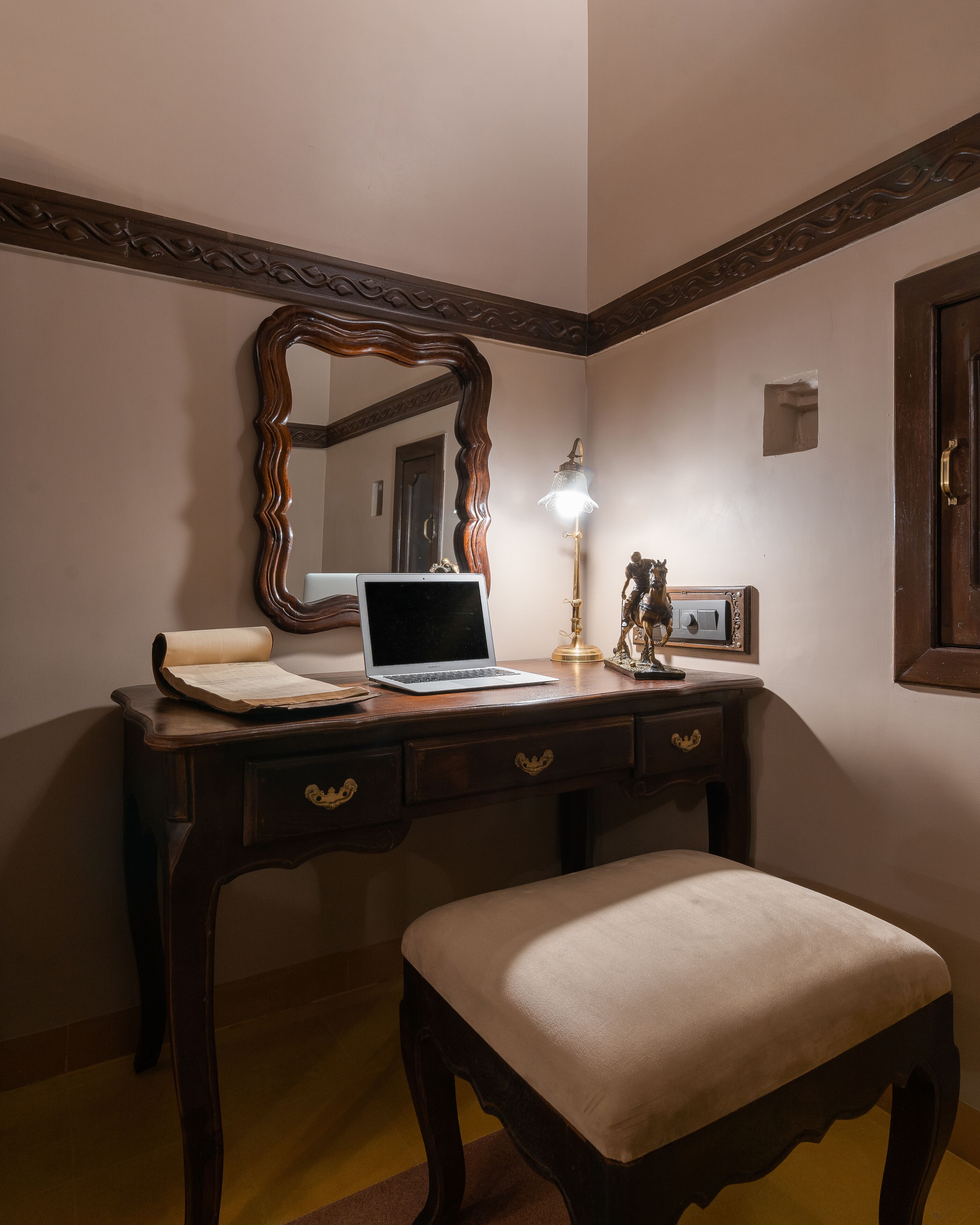 A wooden desk with a laptop, a lamp, and a statue.