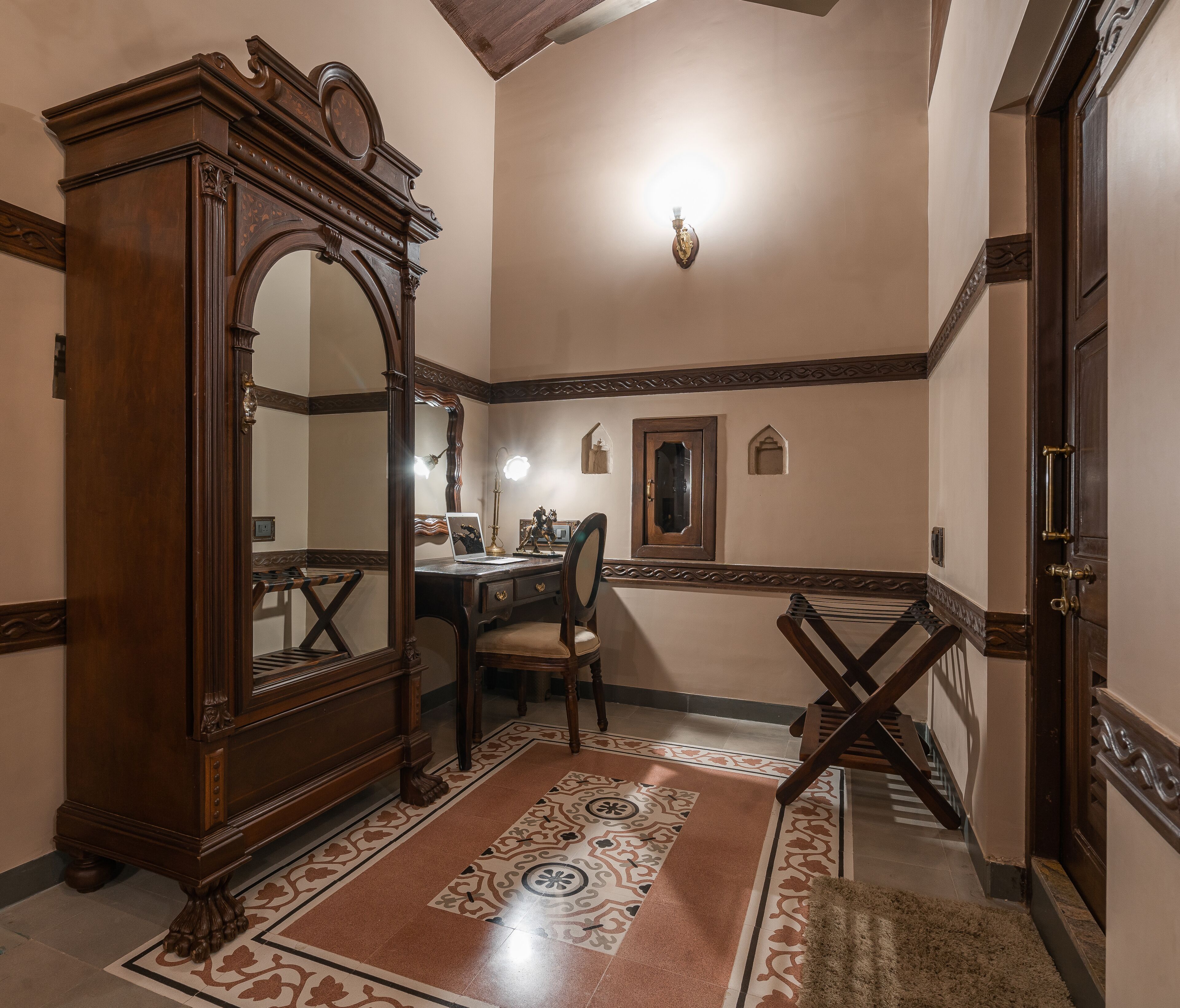 A room with a wooden desk, a chair, a large mirror, and a patterned rug.
