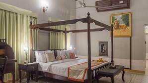 A four-poster bed with a canopy, a bedside table, a nightstand, a framed picture of a lion, and a ceiling fan. - Tree of Life Darbargadh, Dared (Vav)