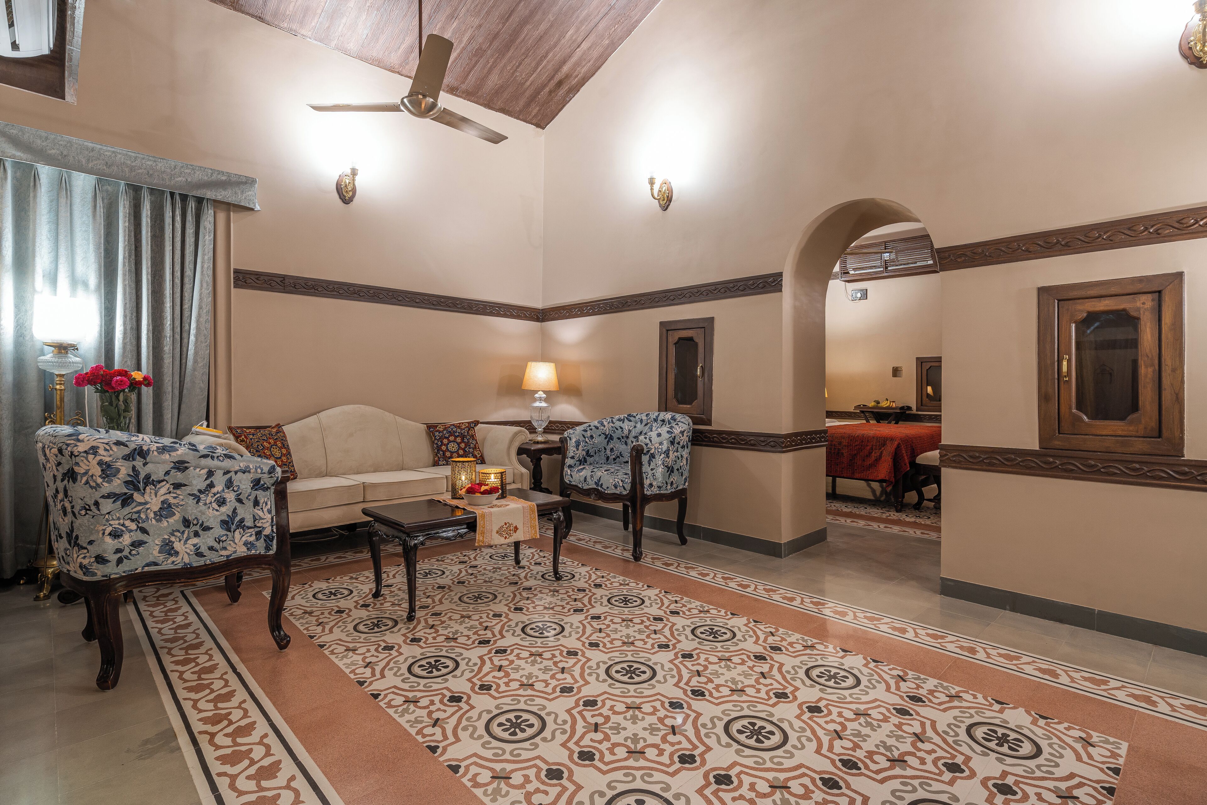 Una sala de estar con un sofá, dos sillones, una mesa de centro, un tapete estampado y una zona de comedor al fondo.