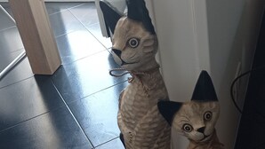 Two cat-shaped sculptures on a dark tiled floor near a doorway.