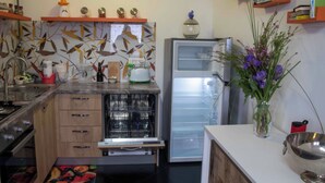 A kitchen with a dishwasher, a refrigerator, and a sink. There are shelves with jars and a vase with flowers.