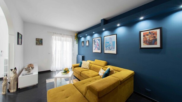 A modern living room with a yellow sofa, a white coffee table, and framed artwork on the walls.
