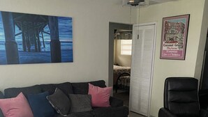 Una sala de estar con un sofá modular, una mesa de centro redonda, un sillón de cuero negro, un ventilador de techo y una obra de arte enmarcada en la pared.