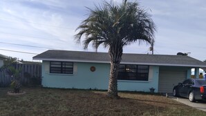 Una casa residencial con una estructura de un piso, un patio delantero con una palmera y un coche estacionado.