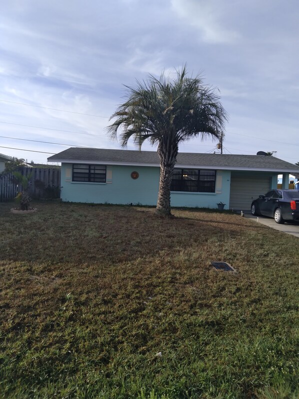 A residential house with a single-story structure, a front yard with a palm tree, and a parked car.