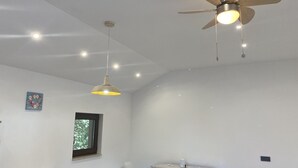 Quarto com mesa de jantar, cadeiras, ventoinha no teto, luminárias pendentes, janela e armário.
