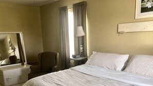 A hotel room with a large bed, a chair, a desk, a lamp, and a dresser. - Rose Ellen’s Country Estate10% saving on 30 day stays  (Leesburg)