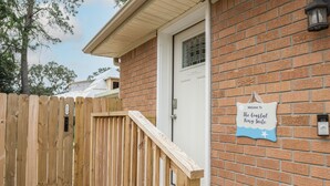 Una cerca de madera con un letrero que dice 'PUSH', un edificio de ladrillo con una puerta blanca, y un cartel que reza 'Welcome to The Coastal King Suite'.