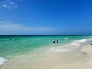 A beach with clear turquoise water, a sandy shore, and a few people in the water.