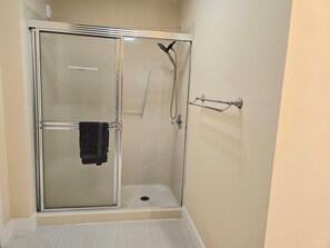 A glass-enclosed shower with a towel rack and a handheld showerhead.