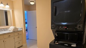 Una cocina compacta con lavadora y secadora integradas, encimera de mármol y un espejo grande sobre el lavabo.