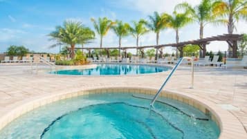 A swimming pool with a circular hot tub, surrounded by lounge chairs and palm trees.