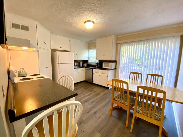 A compact kitchen with white cabinets, a stove, a microwave, and a dining area with a table and chairs.