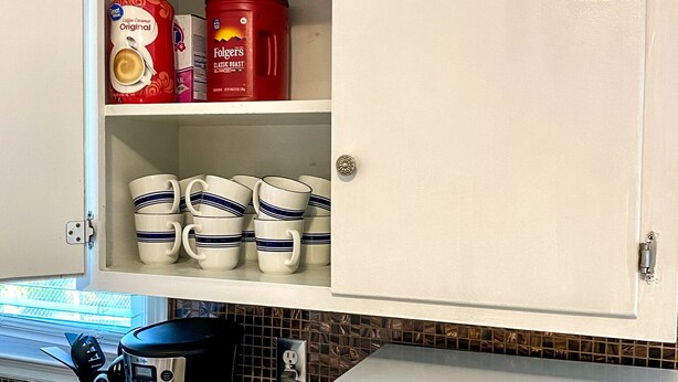 A kitchen with a coffee maker, a microwave, and a cabinet containing coffee cups and Folgers coffee. - Cozy Ranch Close to everything (Merriam)