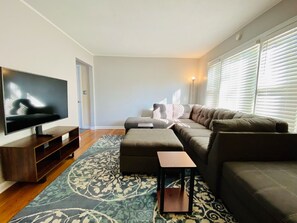 Una sala de estar moderna con un televisor de pantalla plana, un sofá modular, un pequeño reposapiés y una alfombra estampada.