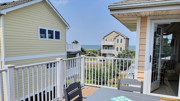 A balcony with a table and chairs, overlooking a beach and other buildings. - Steps From The Beach and Minutes to The Boards - Now Includes Linens (Milton)