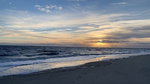 A beach with footprints leading to the water, a clear sky, and the sun setting over the horizon. - Steps From The Beach and Minutes to The Boards - Now Includes Linens (Milton)