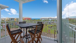 En balkon med bord og stole, med udsigt over et resortområde med bygninger og havudsigt.