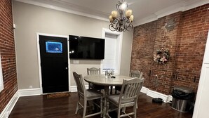 Uma área de refeições com uma mesa redonda, seis cadeiras, um lustre, uma TV de tela plana e uma parede de destaque em tijolos.
