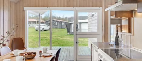 Eine moderne Küche mit einem großen Fenster, einem Essbereich mit Tisch für zwei Personen und Blick auf eine Wohngegend.