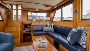 A cozy interior with a wooden bench, a small table, and a window overlooking a marina. - Spacious & Comfy 2BR/2Bath Yacht -Toasty Heat- On Freedom Trail-Walk to Downtown (Boston)